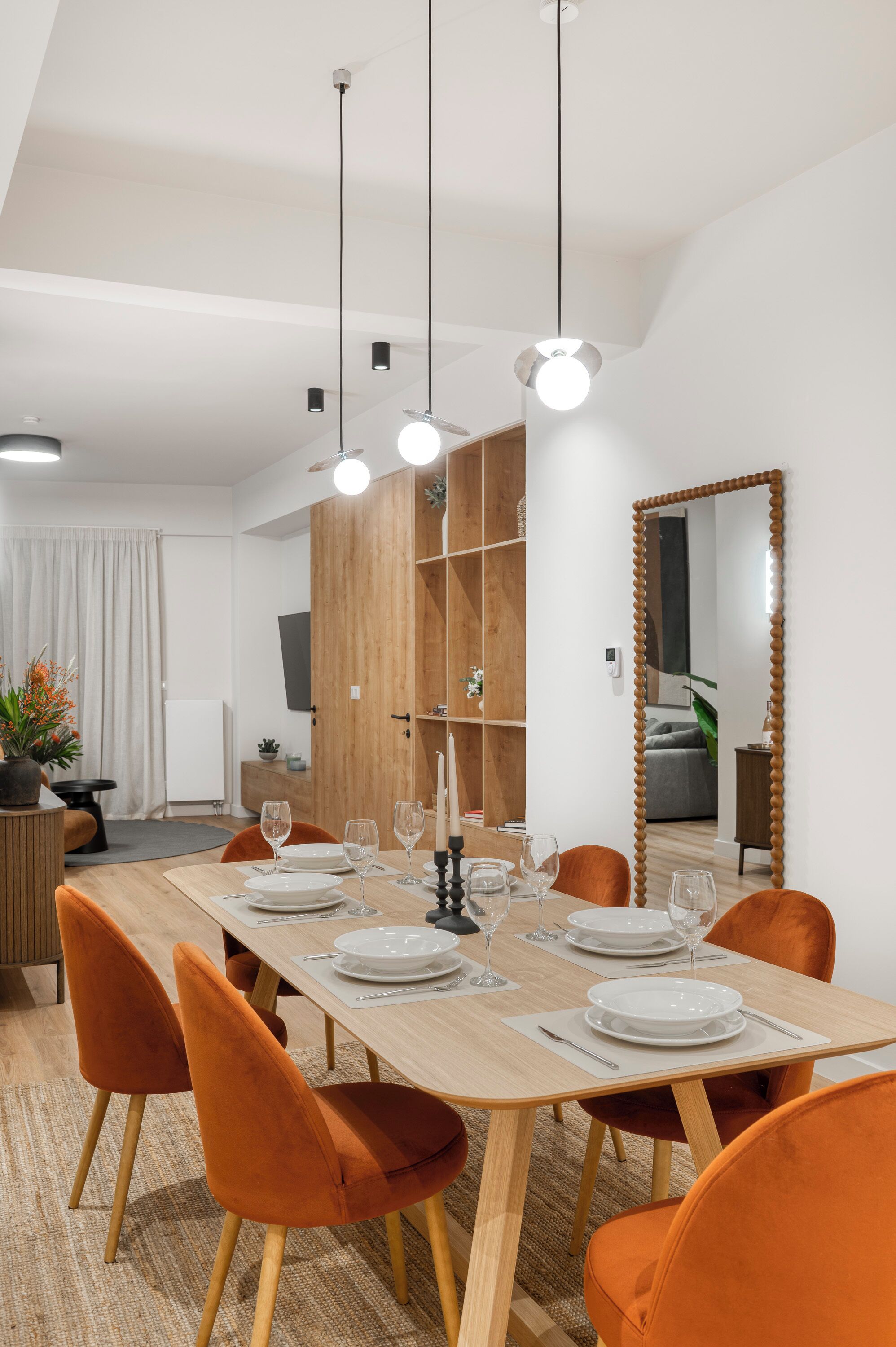 A dining area with a wooden table set for six, orange chairs, and pendant lighting.