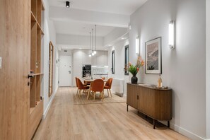 A modern kitchen with white cabinets, a dining area with a wooden table and orange chairs, and a wooden cabinet with a vase of flowers. - Spacious Modern Apartment- Heart of Glyfada Center (Glifada)