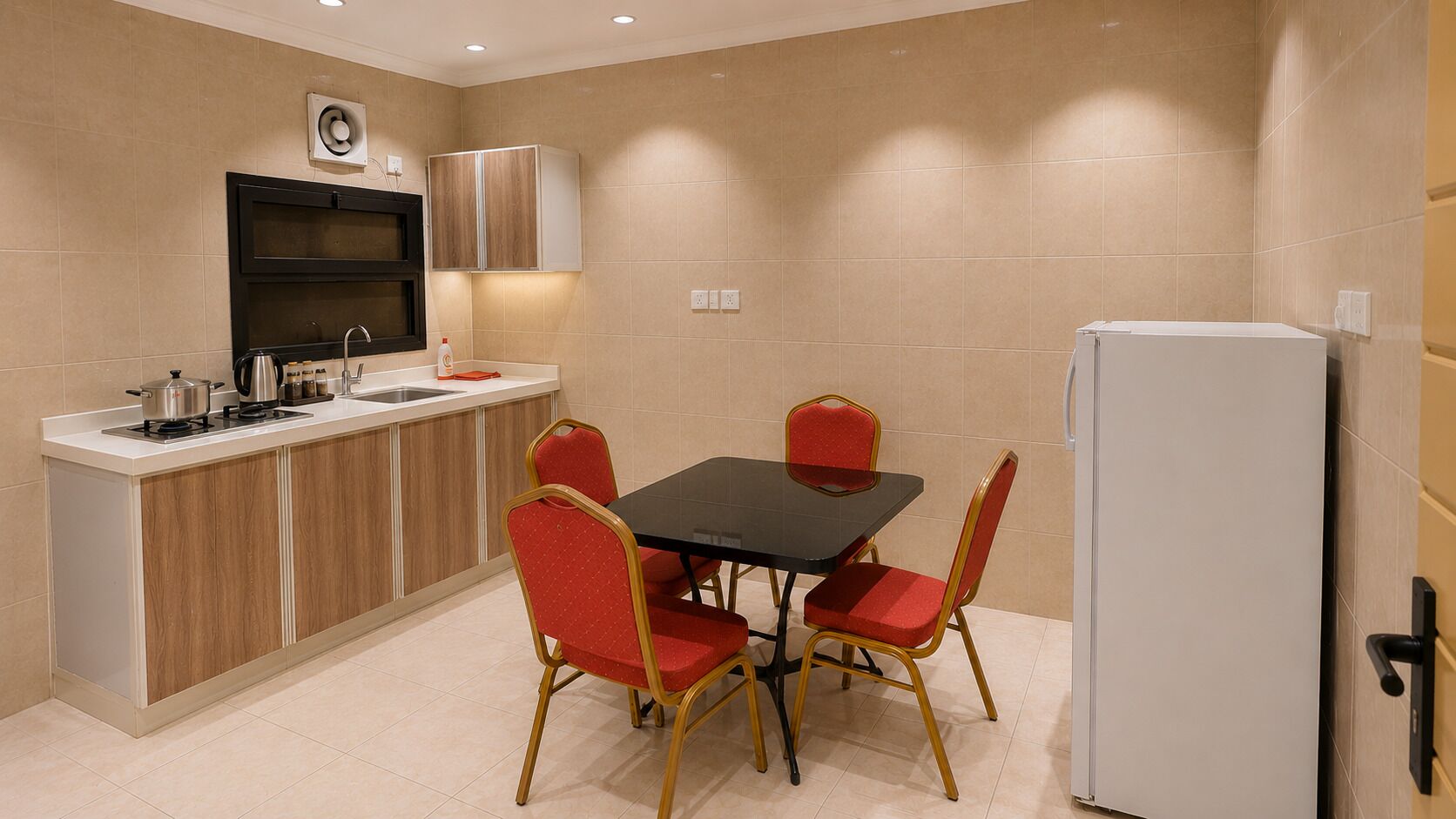 A compact kitchen with a dining table and chairs, a refrigerator, and a built-in oven.