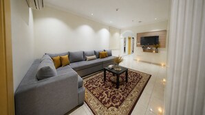 A modern living room with a grey sectional sofa, a small coffee table, and a decorative rug. - AMCO Serviced Apartments (Jeddah)