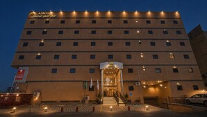 A multi-story hotel with a prominent AMCO sign, a central entrance with steps, and a flag display. - AMCO Serviced Apartments (Jeddah)