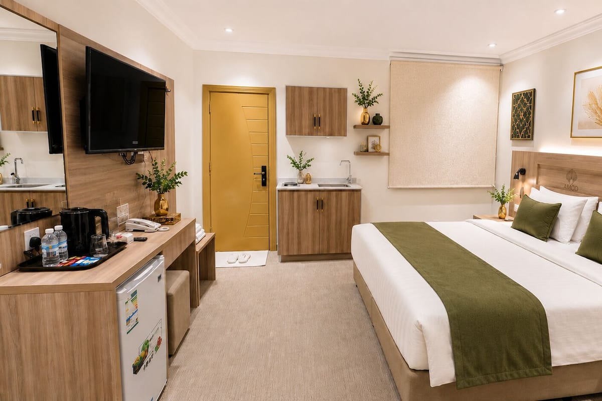 Una habitación de hotel con cama, escritorio con cafetera, televisor y baño con inodoro y lavamanos.