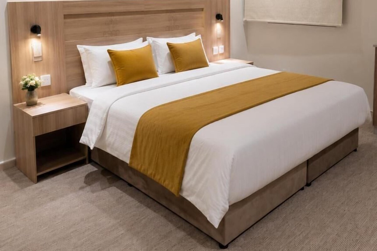 A hotel room with a large bed, bedside tables, and wall-mounted lighting.