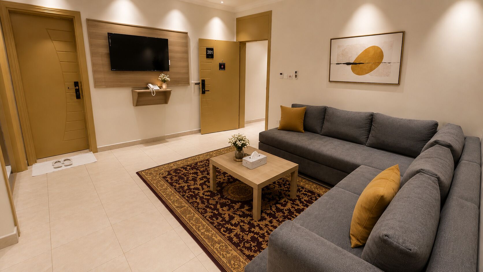 Una sala de estar moderna con un sofá gris, una mesa de centro de madera, un televisor instalado en la pared y una alfombra estampada.