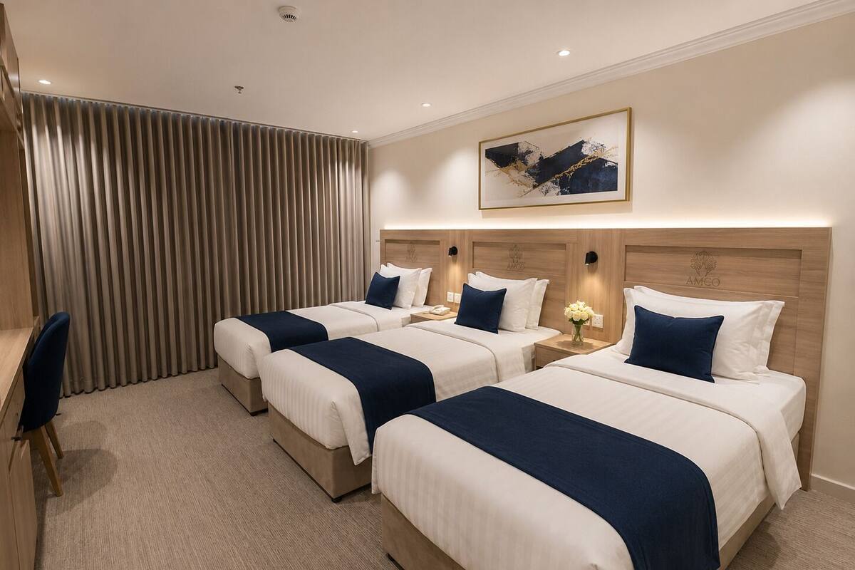 Habitación de hotel con tres camas, un escritorio y un ventanal con cortinas.