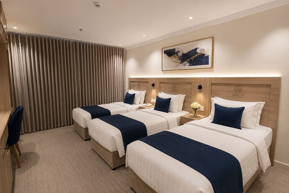 Ett hotellrum med tre sängar, ett skrivbord och ett stort fönster med gardiner.