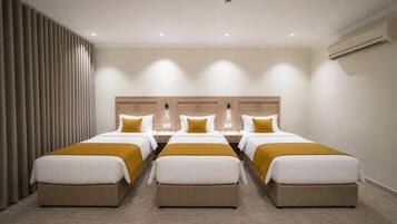 Een hotelkamer met vier bedden, een groot raam met gordijnen, een airconditioning en een wandlamp.