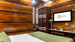 Une chambre d’hôtel équipée d’un lit, d’un ventilateur de plafond, d’un climatiseur, d’un bureau agrémenté d’un vase de fleurs et d’un logo encadré au mur.