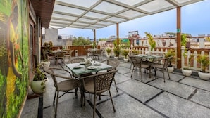 Une terrasse extérieure avec des tables et des chaises, des plantes en pot et une vue sur le paysage urbain.