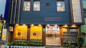 Un hôtel avec une enseigne indiquant « HÔTEL RODALI », doté d’une façade moderne avec un toit plat, de nombreuses fenêtres et une entrée bien éclairée.