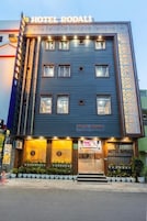 Un hotel con un cartel que dice 'HOTEL RODALI', que presenta una fachada moderna con techo plano, múltiples ventanas y una entrada bien iluminada.
