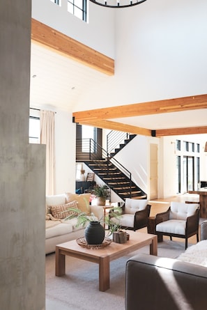 A spacious living area with a high ceiling, a staircase, and a view of the outside. - Group destination! 19 beds. Basketball/pickleball court/hottub/sauna/coldplunge. (Monroe)
