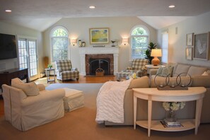A living room with a fireplace, two armchairs, a sofa, a coffee table, and a TV. - Modern upscale 5 bedroom home, close to Mayflower Beach! (Dennis)