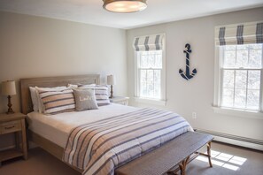 A bedroom with a bed, bedside tables, a bench, and two windows with curtains. - Modern upscale 5 bedroom home, close to Mayflower Beach! (Dennis)