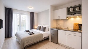 Una habitación de hotel moderna con una cama, mesita de noche y kitchenette.