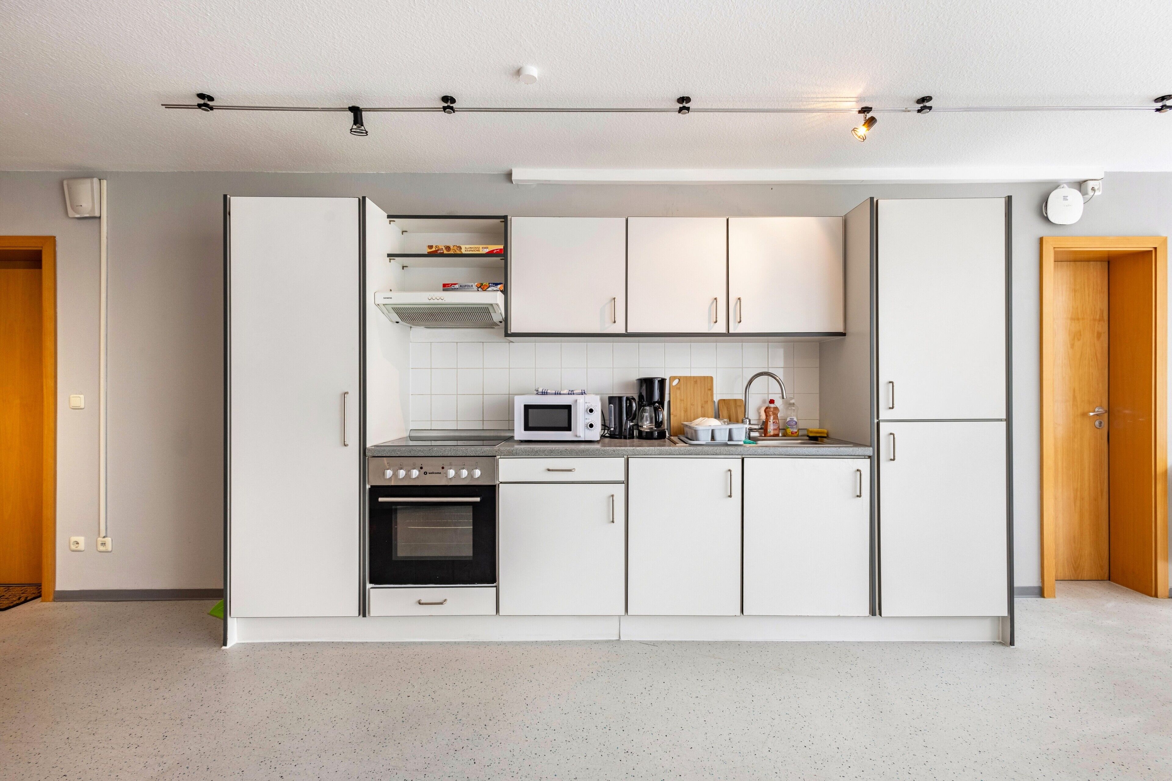 A modern kitchen with white cabinets, a microwave, a stove, and a coffee maker.