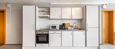 A modern kitchen with white cabinets, a microwave, a stove, and a coffee maker.