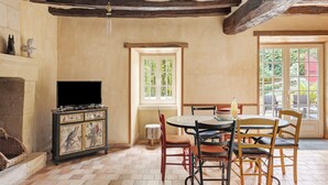 A dining area with a round table, chairs, a television, and a fireplace.