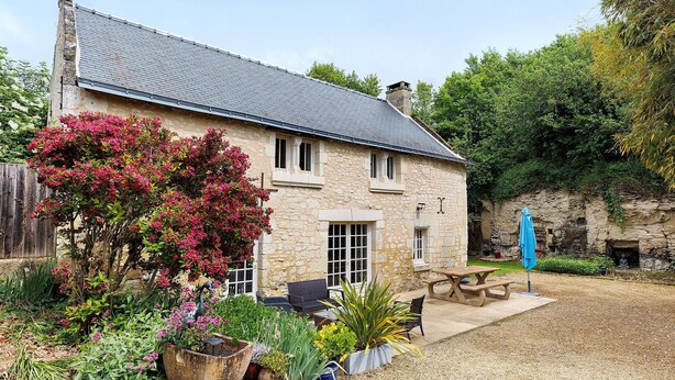 A stone house with a gravel patio, outdoor seating, and a variety of plants.