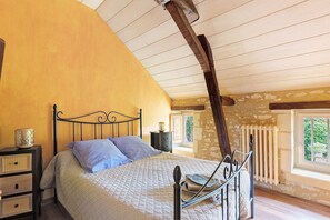 Ein Schlafzimmer mit Bett, Nachttischen, einem Fenster und einer Steinwand.