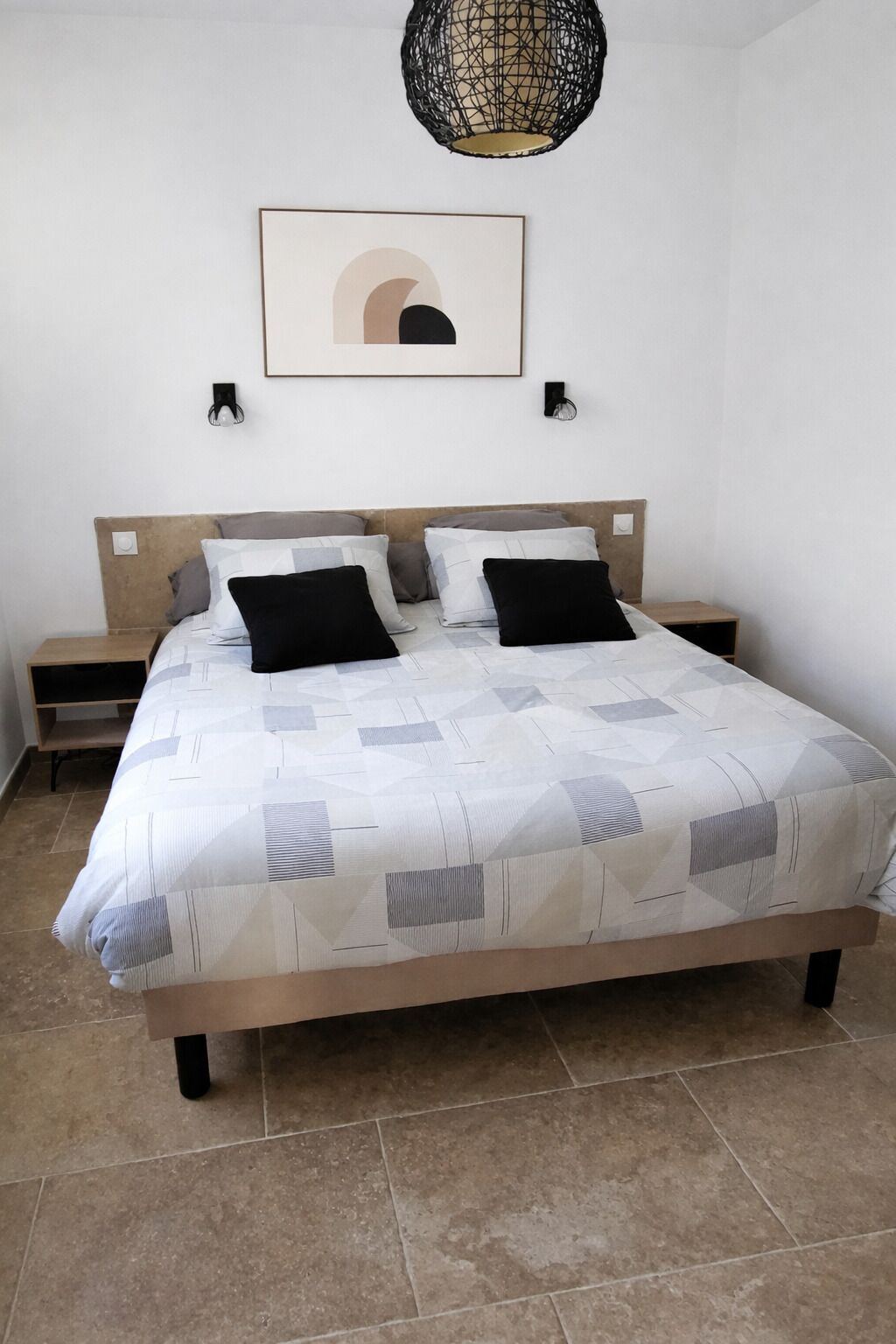 Quarto com cama, duas mesas de cabeceira, luminária na parede e pendente.
