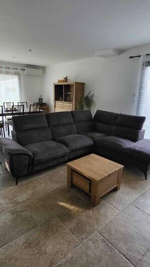 Ein Wohnzimmer mit einem Ecksofa, einem Holztisch, einer Kommode und einem Essbereich.