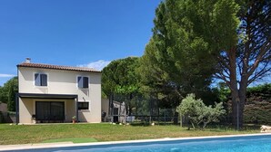Et hus med swimmingpool, en overdækket terrasse og et stort træ.