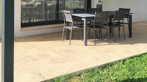 En overdækket terrasse med et bord og stole, store skydedøre i glas og et lille vindue.