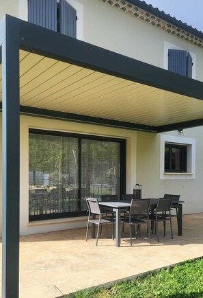 Eine überdachte Terrasse mit Tisch und Stühlen, großen Schiebeglastüren und einem kleinen Fenster.