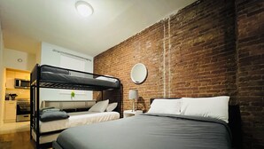 A room with a bunk bed, a round mirror, a bedside table with a lamp, and a kitchen area in the background. - Grand Upper West Side Suite, Sleeps 8+, Steps to Central Park (New York)