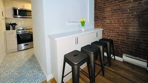 A compact kitchen with modern appliances, a white countertop, and a brick wall. - Grand Upper West Side Suite, Sleeps 8+, Steps to Central Park (New York)