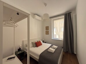 Ein Schlafzimmer mit Bett, Nachttisch, Lampe und einem Fenster mit Vorhängen.
