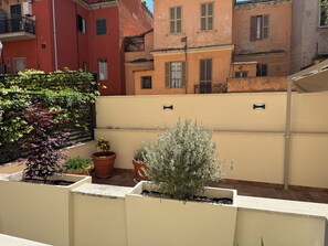 Eine Dachterrasse mit Topfpflanzen, einer weißen Wand und angrenzenden Gebäuden.