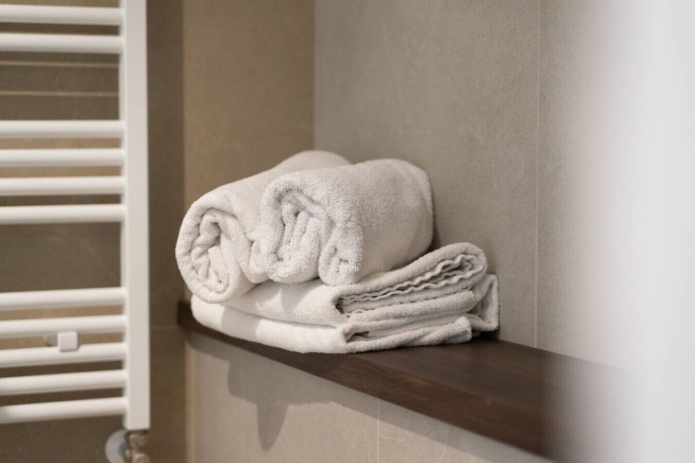 A stack of white towels on a wooden shelf in a bathroom.