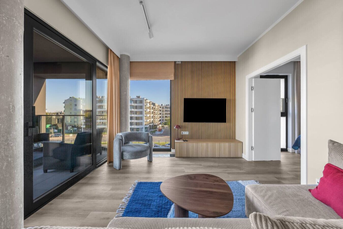 Una sala de estar moderna con un televisor grande, un sofá, una mesita de centro y vistas a la ciudad.