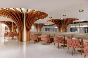 Un interno moderno caratterizzato da colonne in legno curve, tavoli rotondi e sedie imbottite rosa.