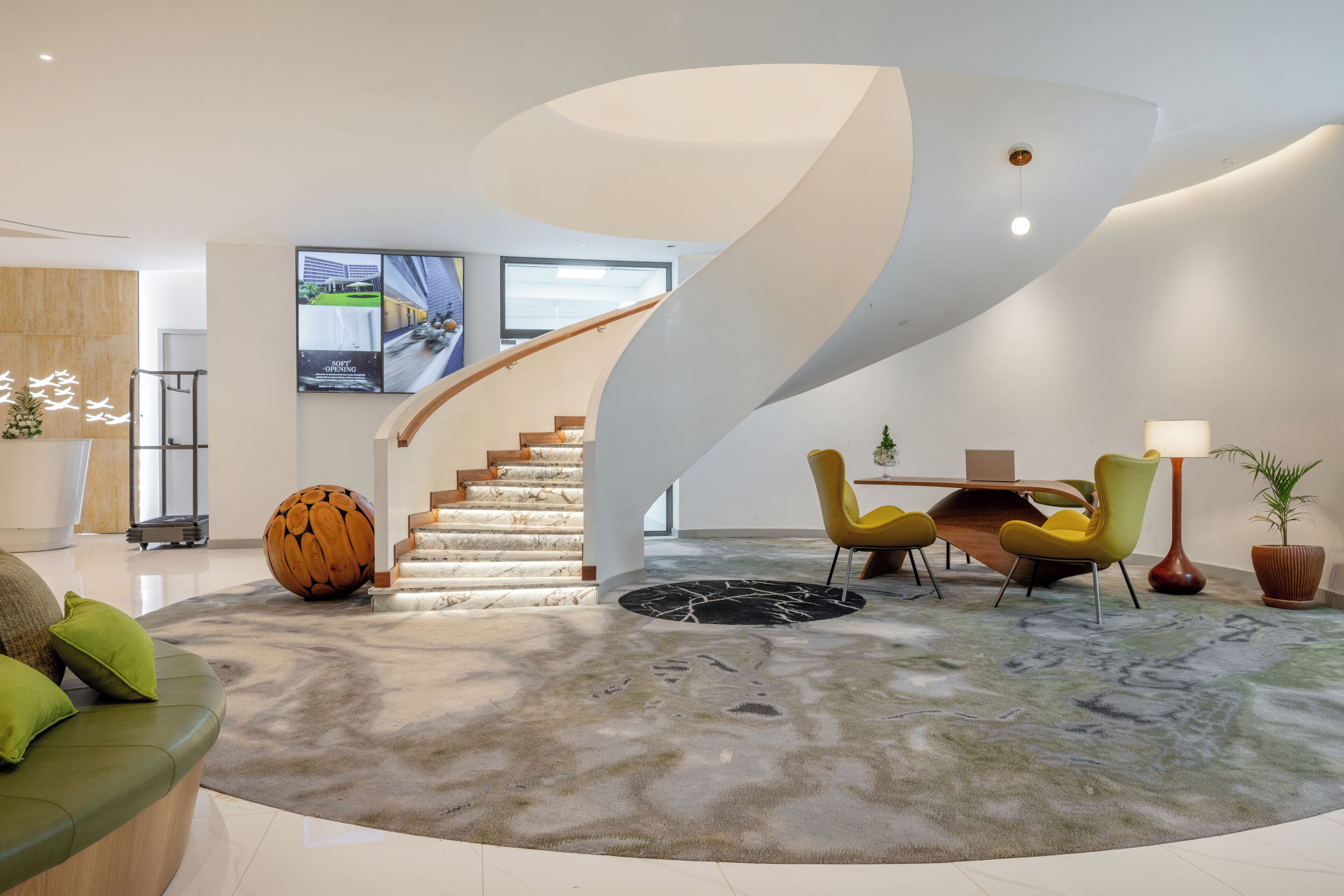 A modern interior with a curved staircase, a round wooden sculpture, and a dining area with yellow chairs.