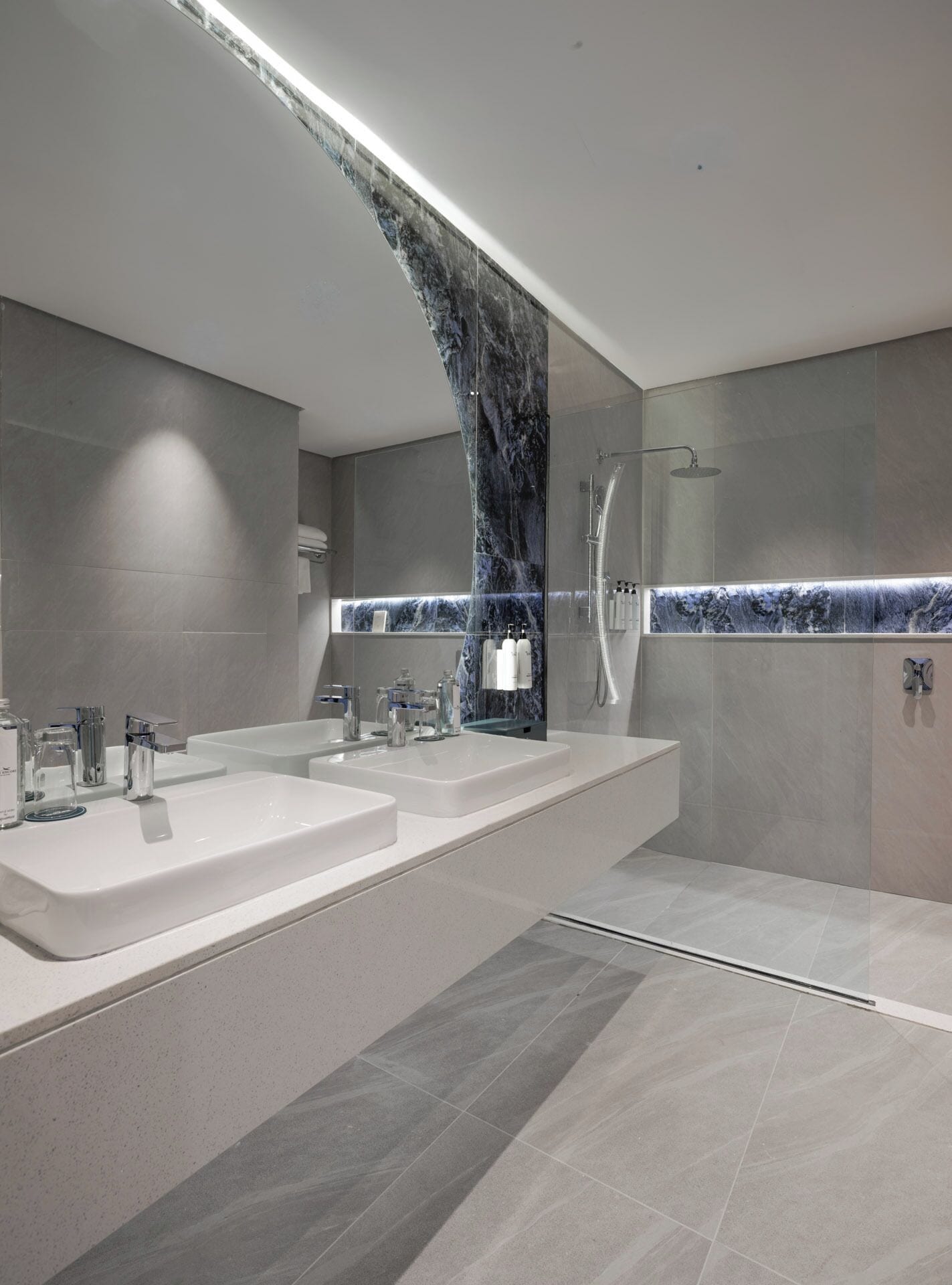 A modern bathroom with a large mirror, two sinks, and a shower area.