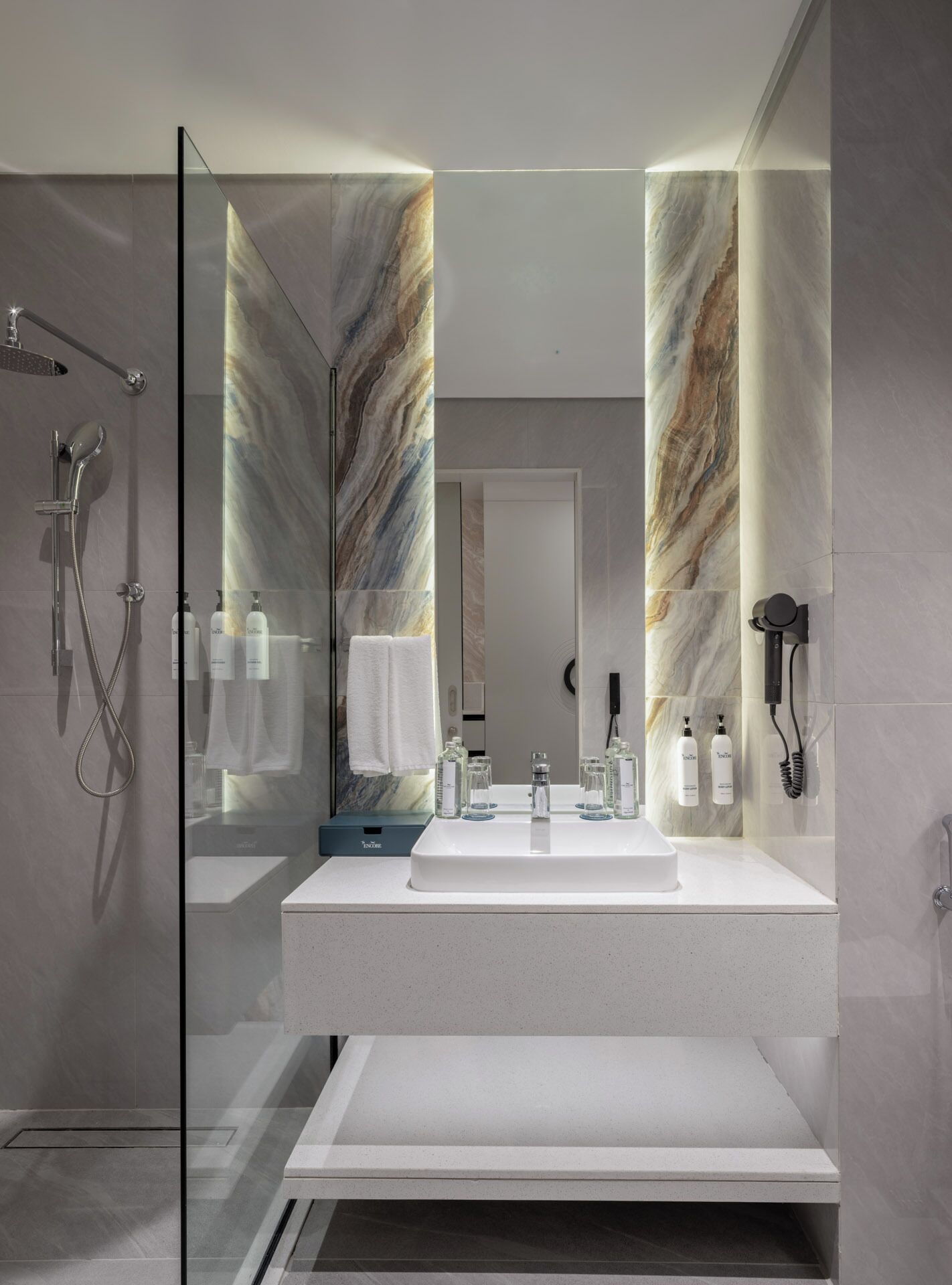 Ein modernes Badezimmer mit einer Duschkabine aus Glas, einem weißen Waschbecken mit Spiegel darüber und Wänden mit Marmoroptik.