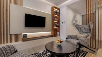 A modern living room with a flat-screen TV, a wooden bookshelf, a round coffee table with fruit, striped sofas, and a patterned rug.