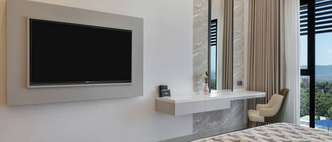 A modern bedroom with a large TV mounted on the wall, a bedside table with a vase, and a view of the outdoors through a window.