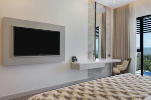 Un dormitorio moderno con un televisor grande montado en la pared, una mesita de noche con un florero, y vistas al exterior a través de una ventana.