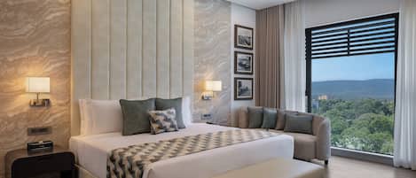 A modern hotel room with a large bed, a sofa, a desk, and a view of the outdoors.