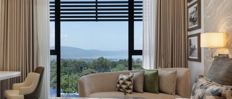 Habitación de hotel con cama, sofá, sillón, escritorio y vistas al exterior.