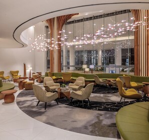 Un área de estar moderna con una disposición de asientos curvada, una mesa de centro de cristal y un candelabro contemporáneo.