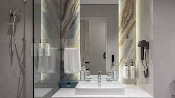 A modern bathroom with a glass-enclosed shower, a white sink with a marble backsplash, and a large mirror.