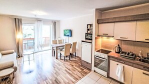 A modern kitchen with a built-in oven, a dining area with a table and chairs, and a living room with a sofa and a TV. - Lovely apartment for 4 people with WIFI, TV and balcony (Finkenstein Am Faaker See)