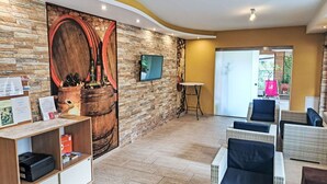 A reception area with a stone wall, a wooden barrel display, a TV, and wicker furniture. - Lovely apartment for 4 people with WIFI, TV and balcony (Finkenstein Am Faaker See)