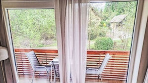 A room with a large window, a wooden deck outside, and a table with chairs. - Lovely apartment for 4 people with WIFI, TV and balcony (Finkenstein Am Faaker See)