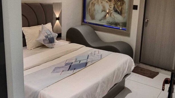 A bedroom with a bed, a wall-mounted air conditioner, a framed picture, and a door. - Hotel Bellemount (Ahmedabad)